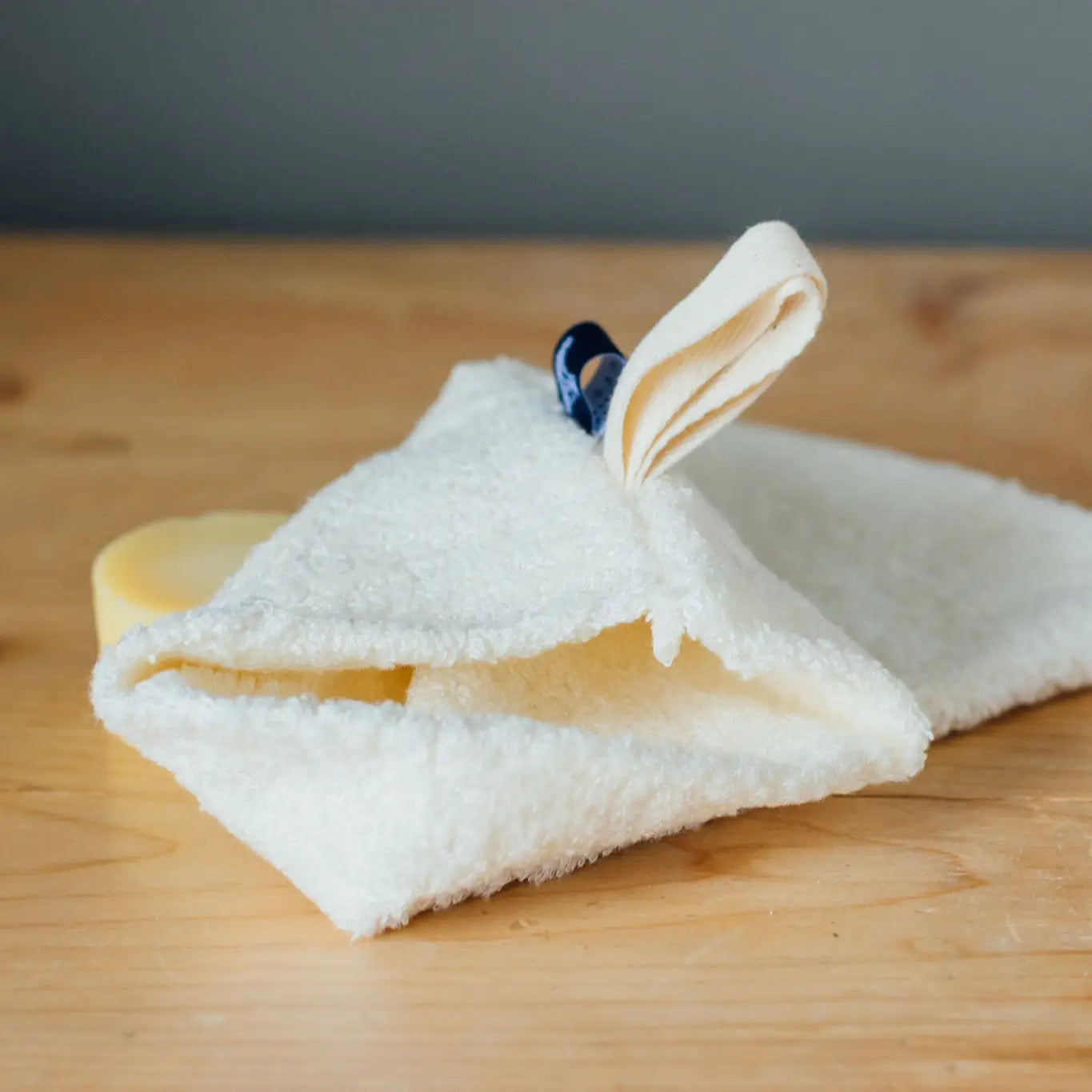 Soft Bamboo Reusable Shower Mitt with hanging loop on wooden surface.