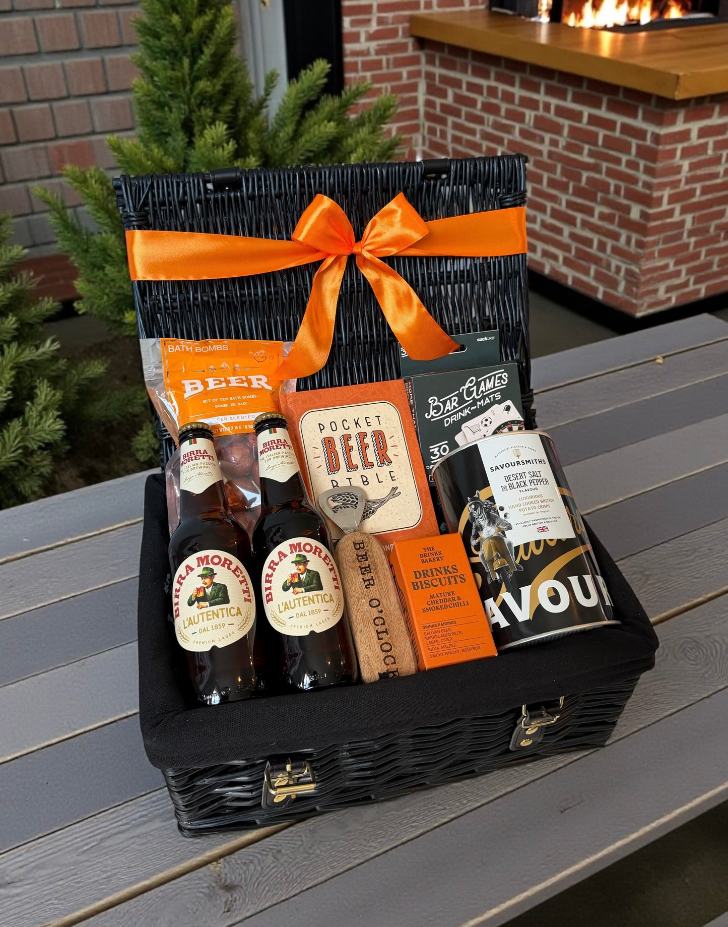 Gift basket with beer bottles and packaging on a wooden surface outdoors.