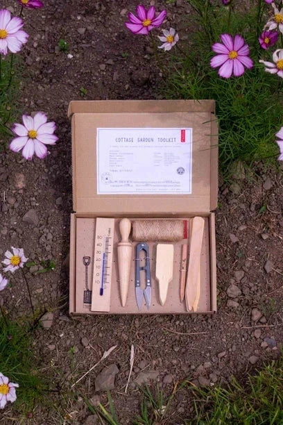 Cottage Garden Tool Kit neatly arranged in an open box on soil with flowers.