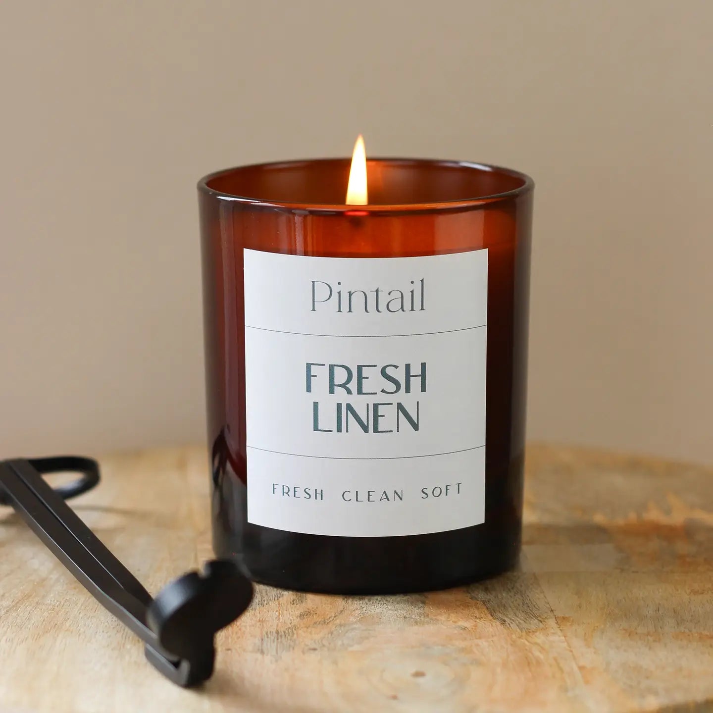 Fresh Linen Glass Candle with soothing floral and musk fragrance in amber jar on wooden surface.