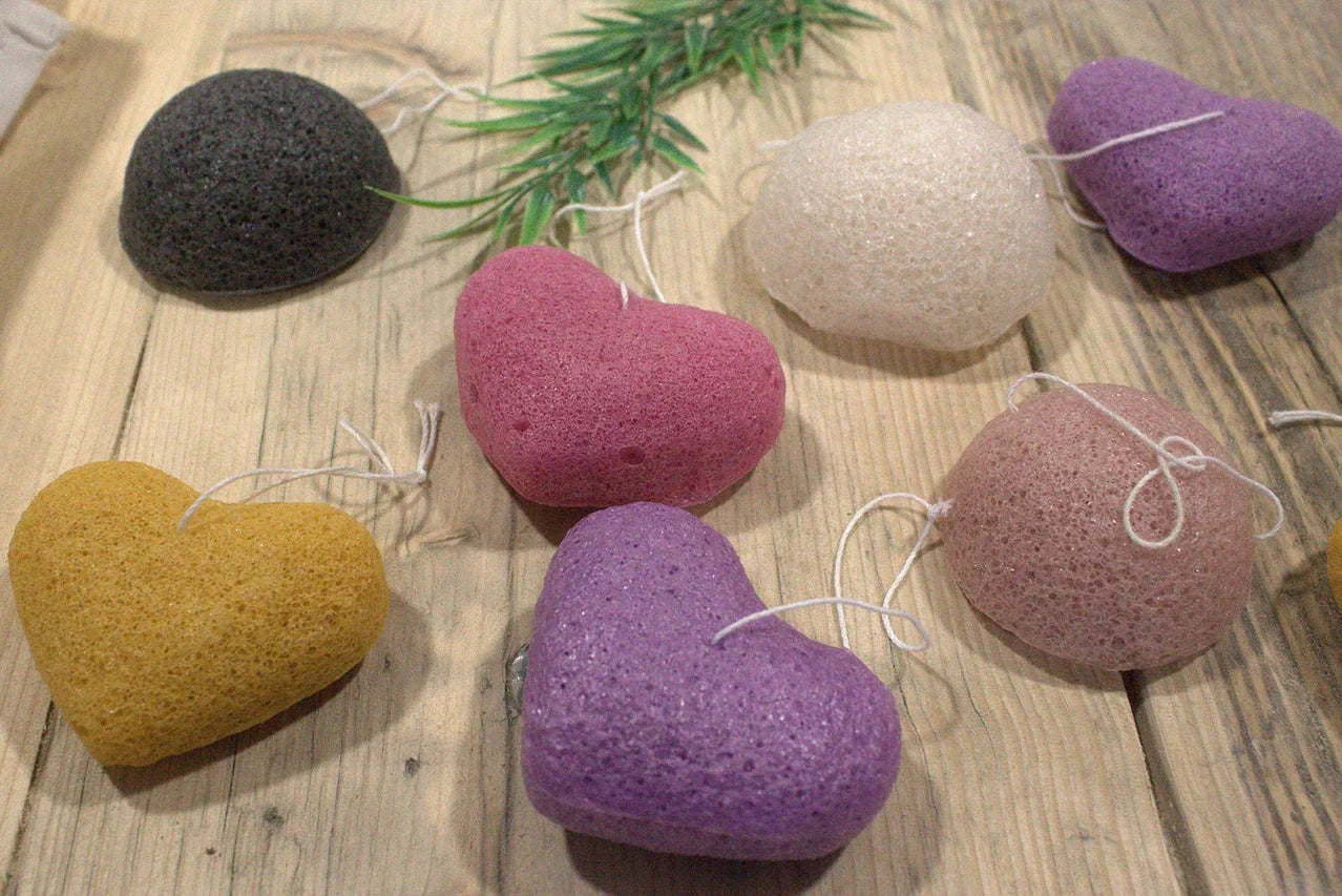 Soft and natural Konjac heart rose sponges in various colors on a wooden surface.