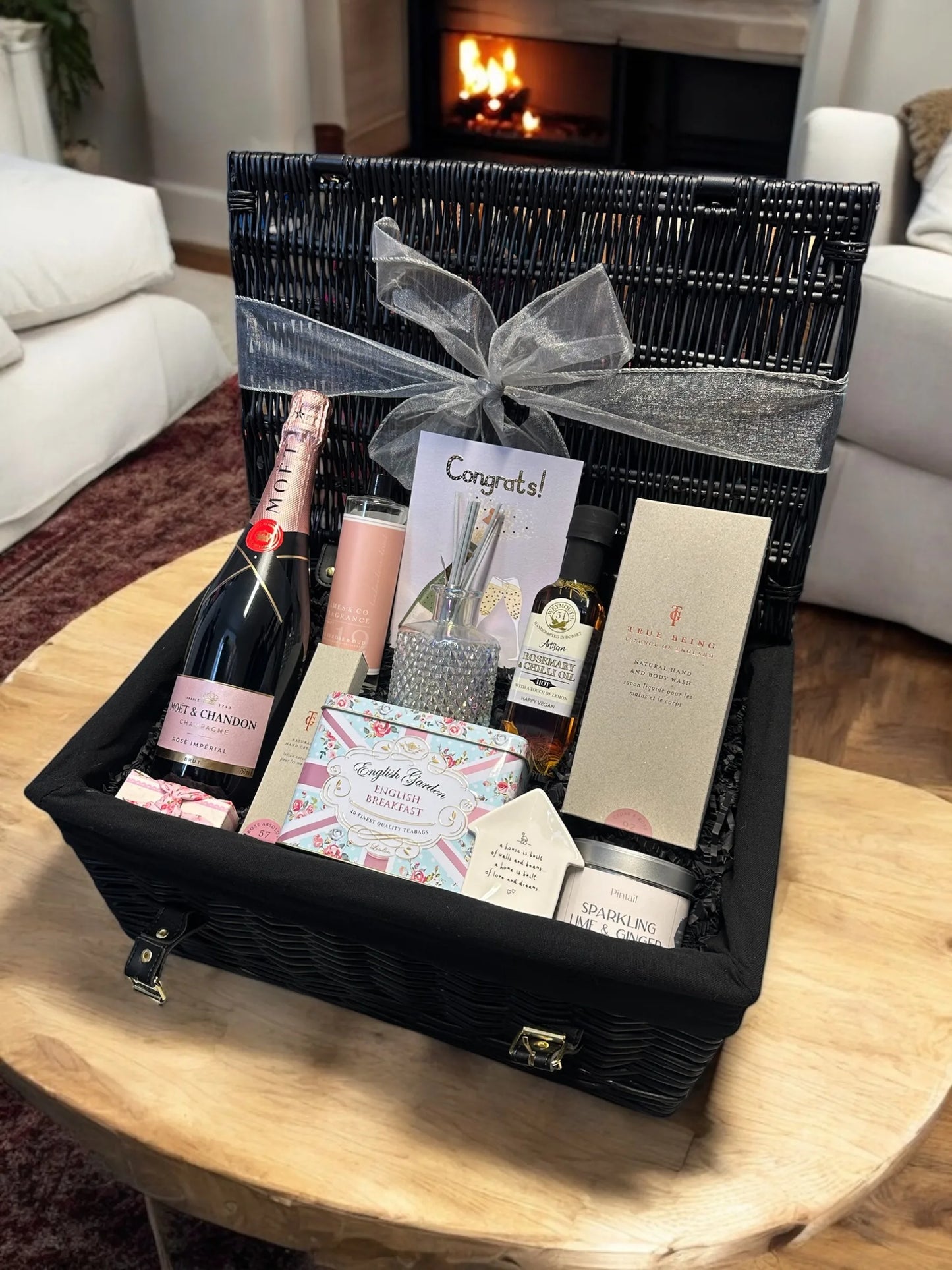 Luxe New Home Celebration hamper with pink Moët Champagne, luxury hand cream, hand and body wash, rose and oud diffuser, tea caddy, gourmet oils, ring dish, fabric-wrapped soap, lime and ginger candle, and a congratulations card.