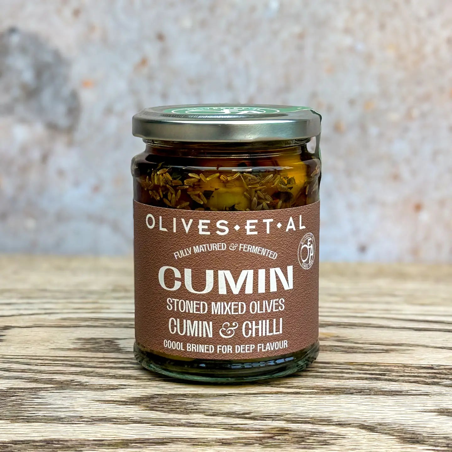 Olives Et Al Cumin Mint Chilli Pitted Mixed Olives jar on wooden surface.