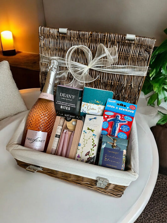Gift hamper with Grow a Boyfriend toy, Freixenet Rosé Prosecco, self-love bath ritual set, Garden Blooms candle, bee-themed notebooks, and savory treats.