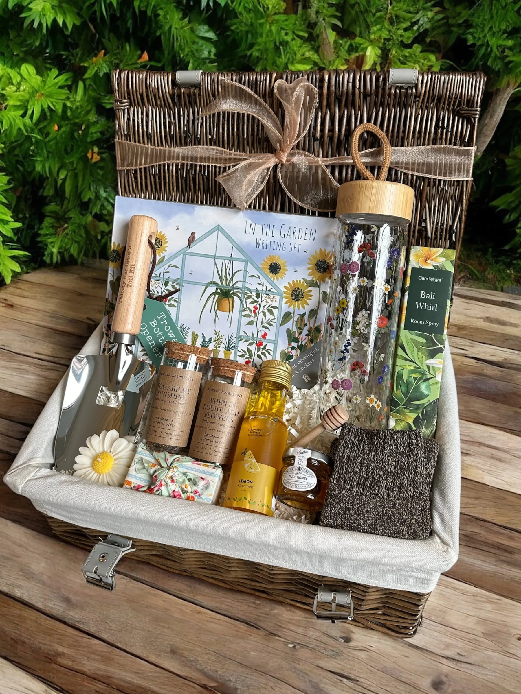 In the Garden hamper with avocado oil, honey set, trowel opener, room spray, writing set, floral soap, daisy candle, and wool socks.