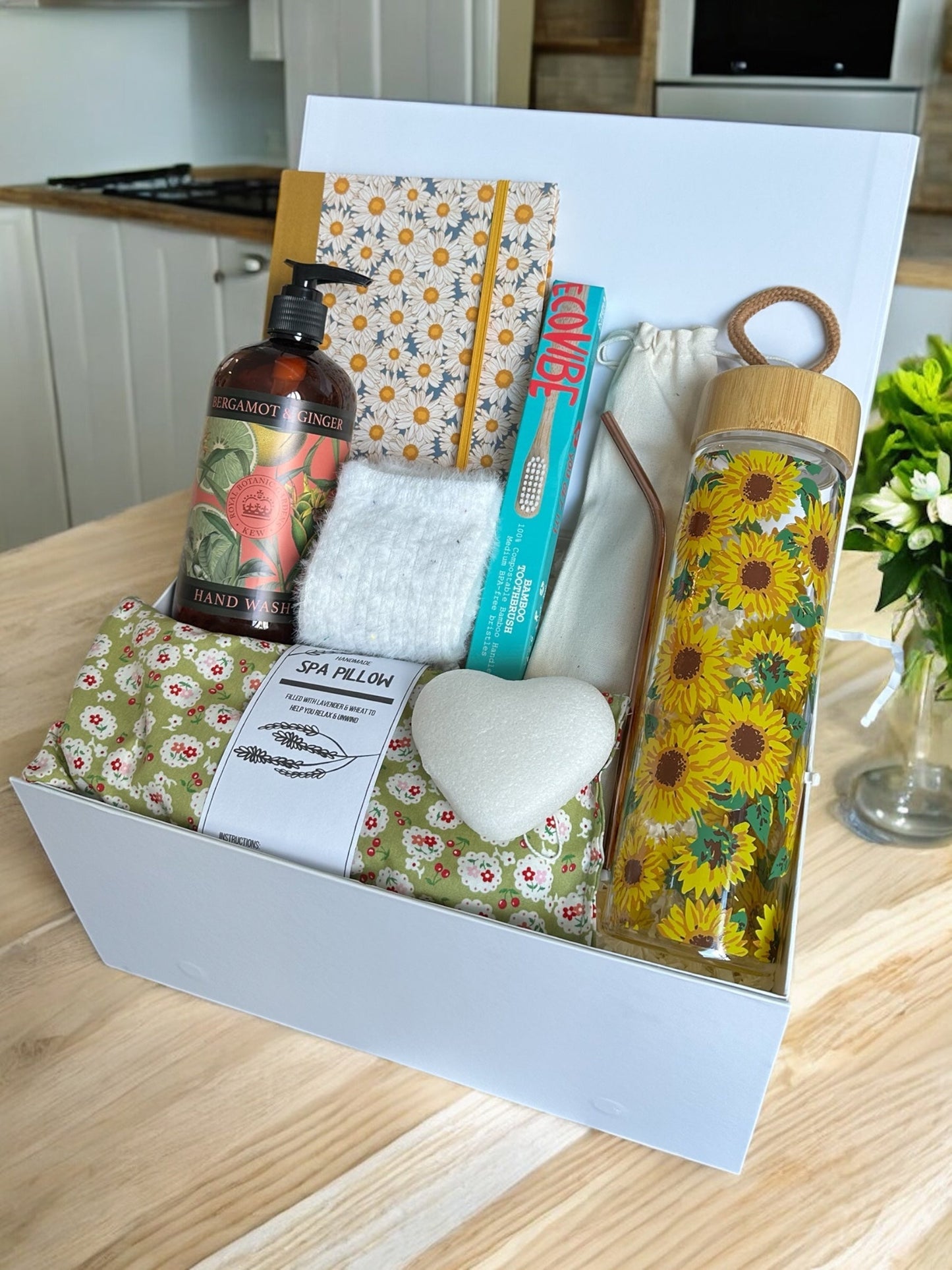 Moving Out Essentials gift box with spa pillow, sunflower water bottle, bamboo toothbrush, steel straws, fluffy socks, Konjac sponge, notebook, and hand wash.