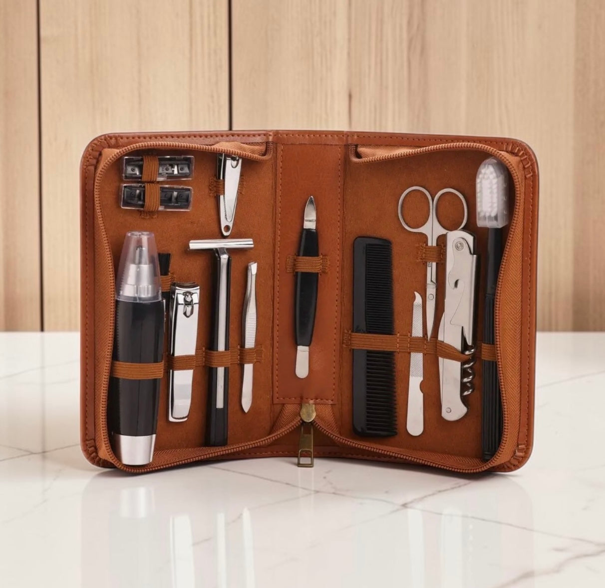 A brown leather grooming kit organizer shown open on a white marble surface with a light wood paneled background. The kit contains multiple grooming tools including scissors, a comb, nail clippers, razors, and other personal care items arranged in elastic pockets.