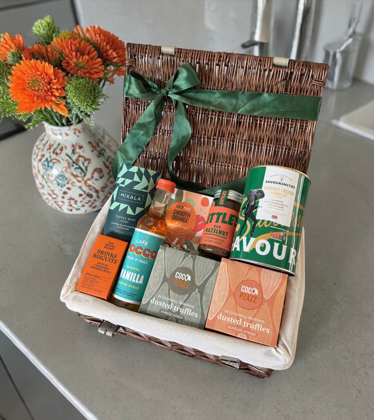 Wicker gift hamper with coffee, chai, truffles, biscuits, syrup and savoury snacks in green and orange theme