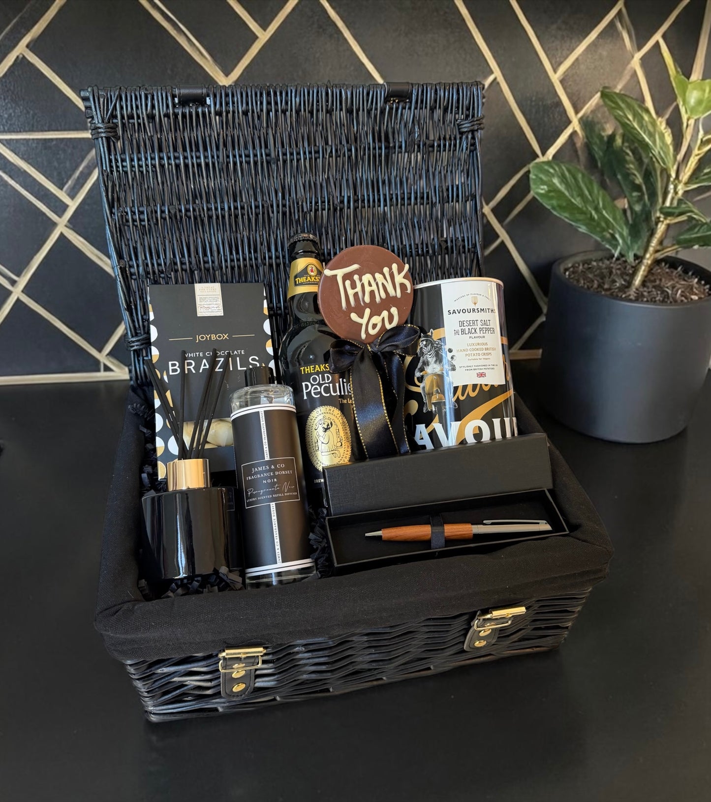 Gift basket with various items on a dark surface with a geometric wall pattern.