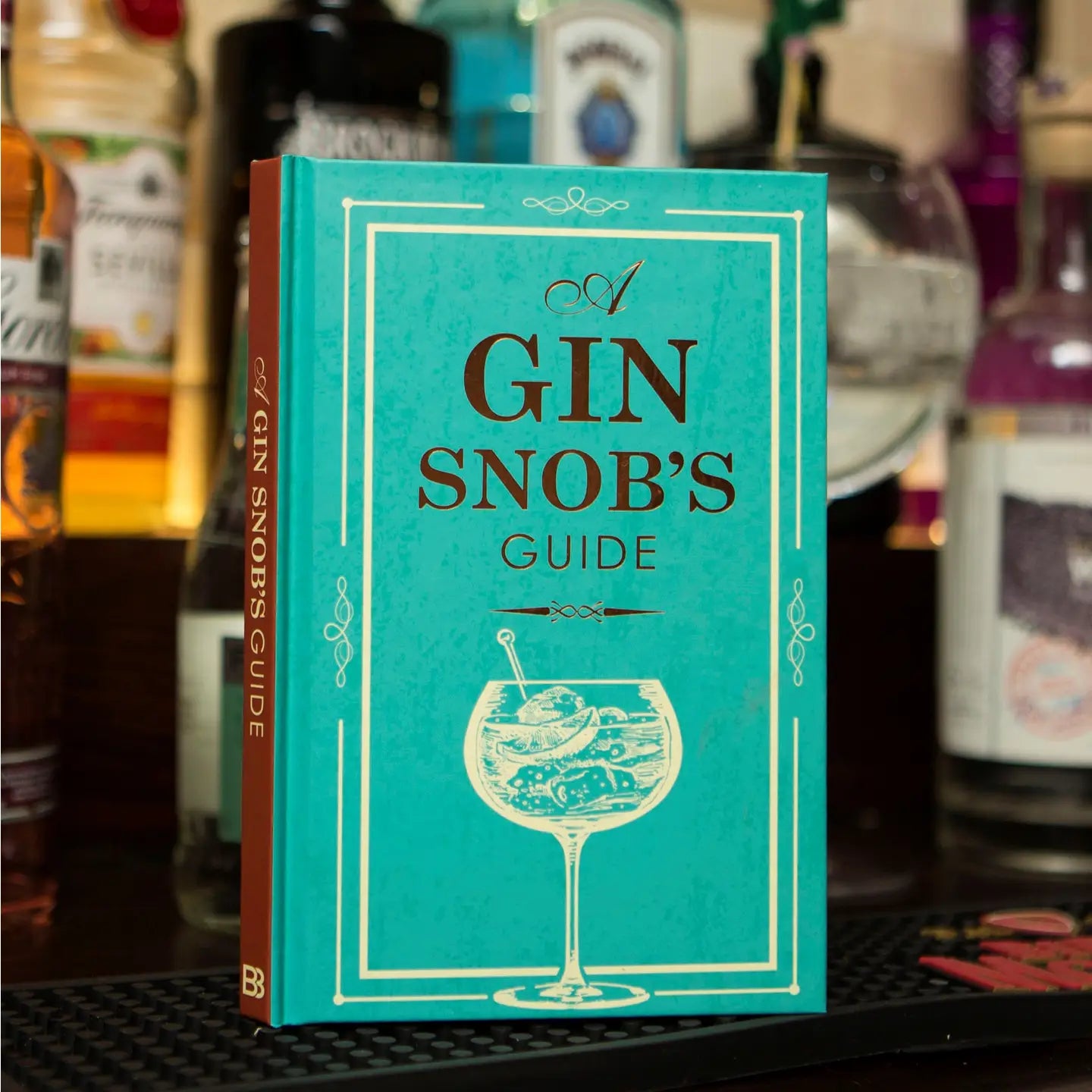 Hardback book titled "A Gin Snobs Guide" with a turquoise cover in a bar setting.