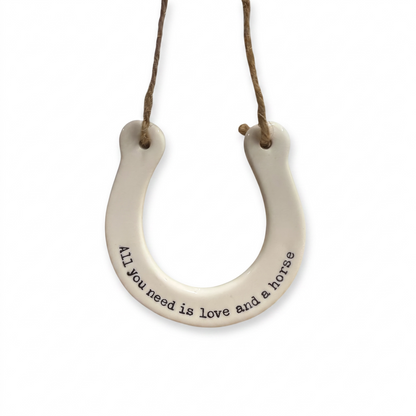White ceramic horseshoe hanging decoration with the quote "All you need is love and a horse" and rustic twine.