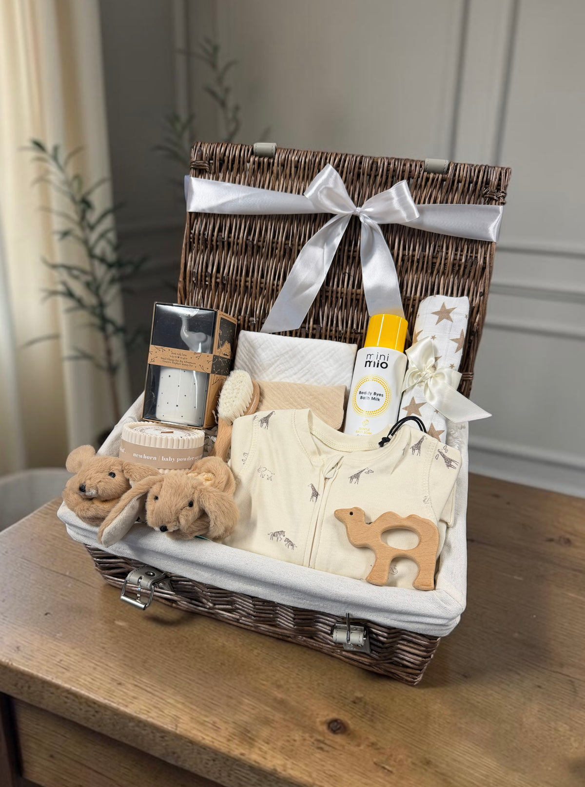Baby Keepsake Safari Hamper with a Safari sleepsuit, bath milk, muslin, bibs, candle, bunny slippers and a wooden teether. A thoughtful new baby gift.