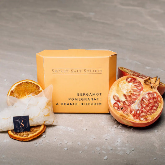 Bergamot, Pomegranate and Orange Mineral Bath Infusion fruit and packaging placed beside.