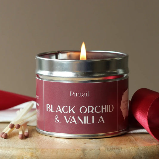 Black Orchid & Vanilla candle in a tin, emitting a warm glow.