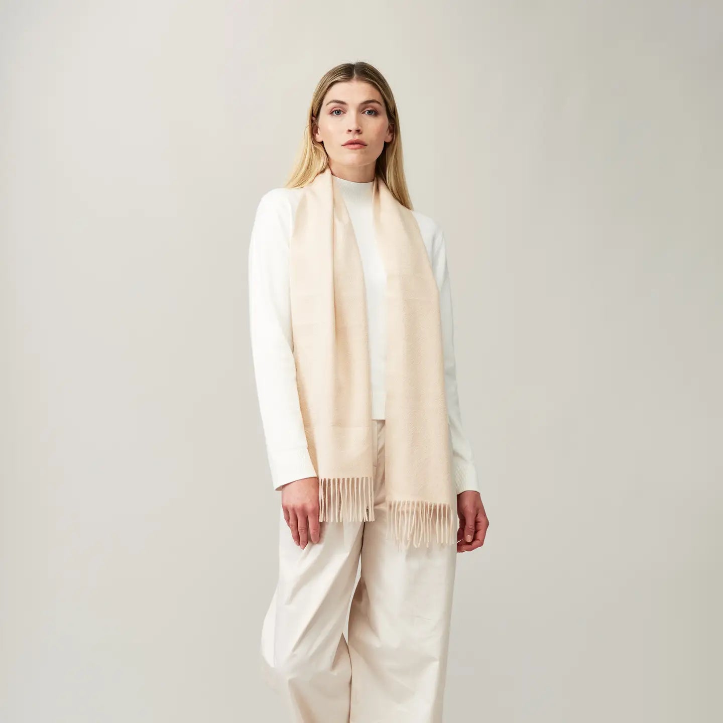 Cashmere scarf in cream color worn by a model, showcasing its soft fringing and smooth texture.