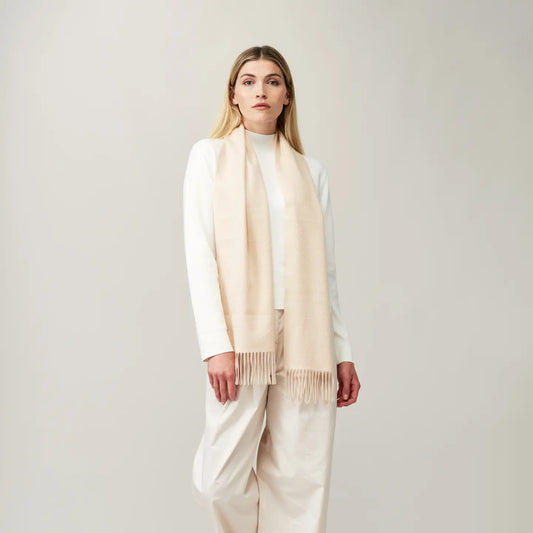 Cashmere scarf in cream color worn by a model, showcasing its soft fringing and smooth texture.