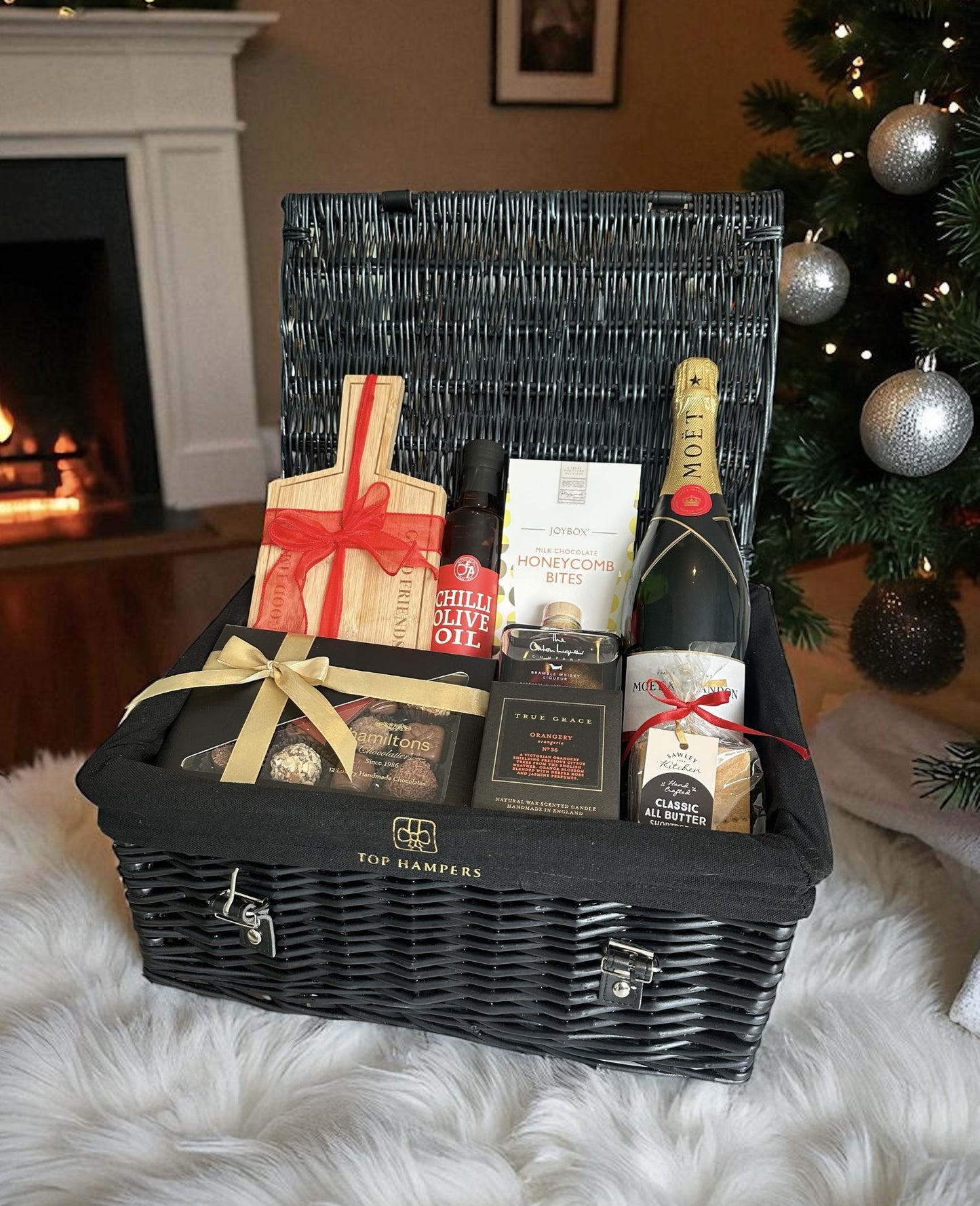 Elegant Christmas hamper with Moët Champagne, True Grace Orangery candle, Oxton Bramble Whisky liqueur, chocolates, shortbread, and serving board.