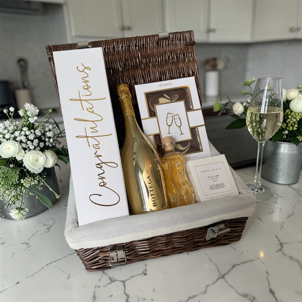 Luxury congratulations hamper with Bottega Gold prosecco, elderflower gin liqueur, True Grace Wild Lime candle and gourmet chocolate in a gold gift box.