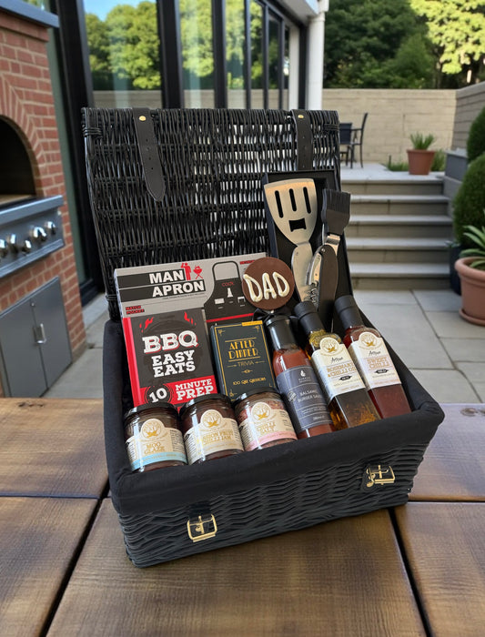 Dad’s BBQ hamper with BBQ apron, sauces, seasonings, personalised BBQ tool, recipe book, chocolate Dad lollipop, and optional drink cans.