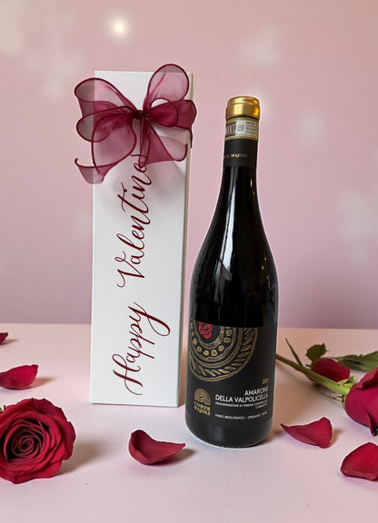 Wine bottle with decorative box and roses on a pink background