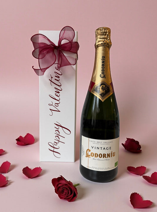 Bottle of Codorniu vintage champagne with a 'Happy Valentine's' gift box on a pink background.