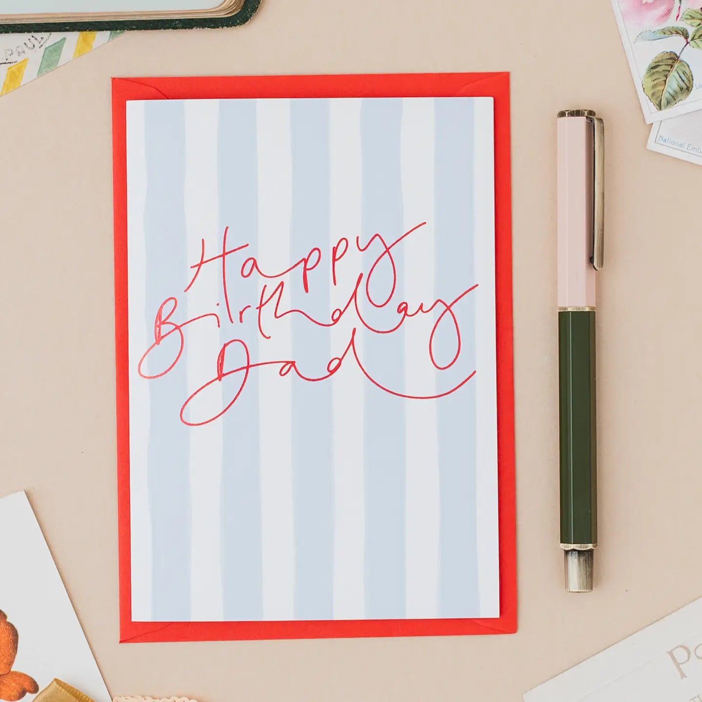 Happy Birthday Dad greetings card with handwritten red lettering on a blue striped background and red envelope.
