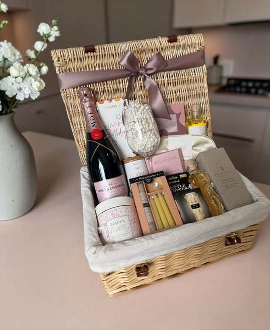 Gift basket with wine, snacks, and candles on a kitchen counter.