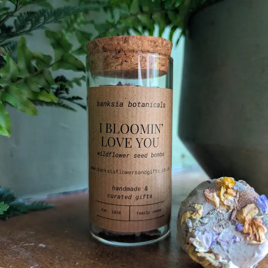 Wildflower Seed Bombs in glass jar with cork lid, surrounded by green plants, labeled "I Bloomin' Love You".
