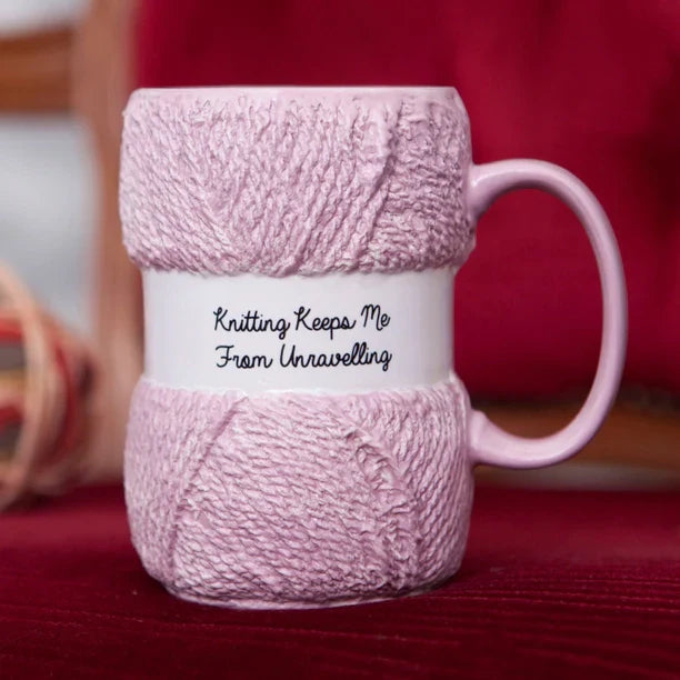 Knitting-themed pink mug with "Knitting keeps me from unravelling" text, shaped like a ball of wool.