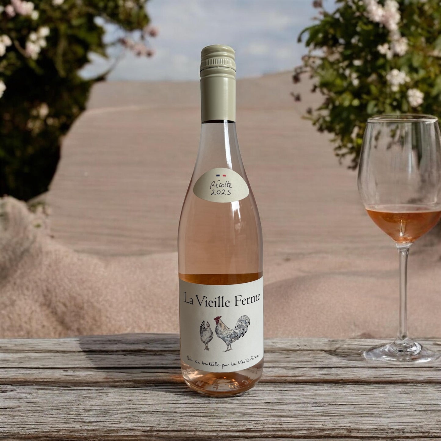Bottle of 'La Vieille Ferme' rosé wine with a glass on a wooden surface outdoors.