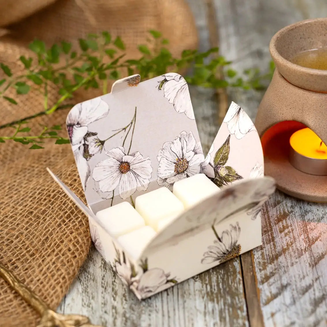 Lime, Basil & Bergamot Soy Wax Melts in floral packaging next to a burning tealight.
