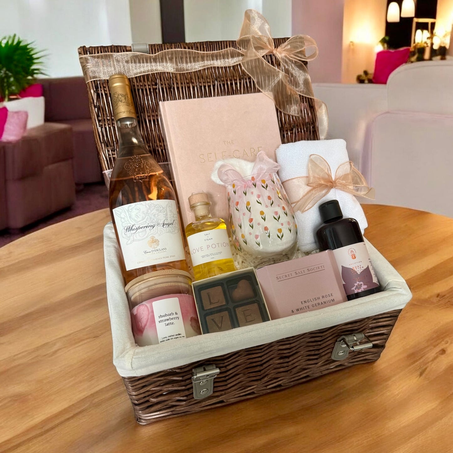 Gift basket with wine, candles, and other items on a wooden table.