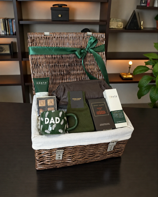 A wicker gift basket with a white liner and green ribbon, filled with dad themed items.