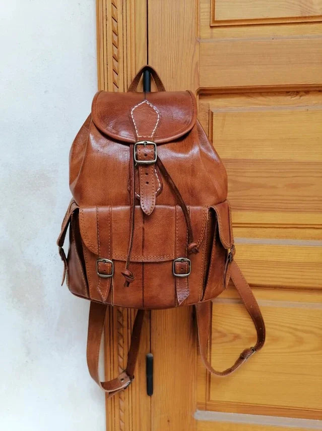 Handmade premium Moroccan brown leather backpack hanging on a wooden door.
