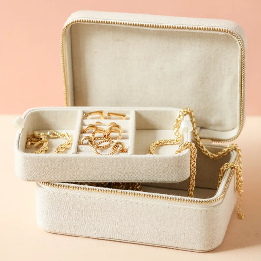Natural linen jewellery case with compartments filled with gold rings and necklaces.