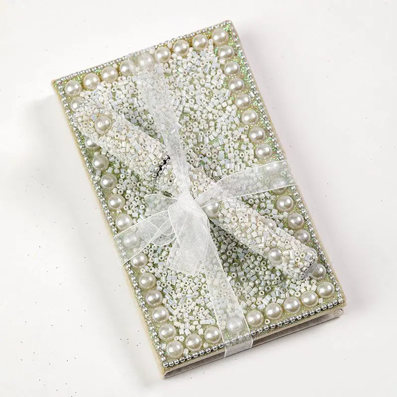 A square embellished box or book-style package decorated with white faux pearls, rhinestones, and a sheer white ribbon tied in a bow, photographed on a plain white background.
