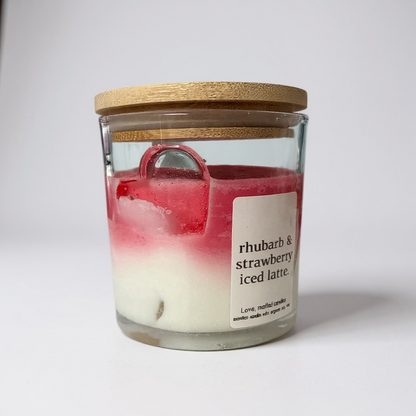 Glass candle with wooden lid labeled 'rhubarb & strawberry iced latte' on a white background