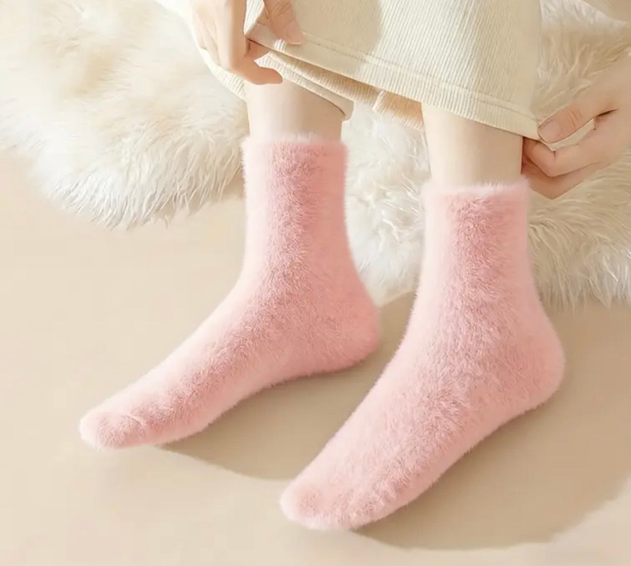Pink fuzzy socks worn by a person sitting on a fluffy white surface.