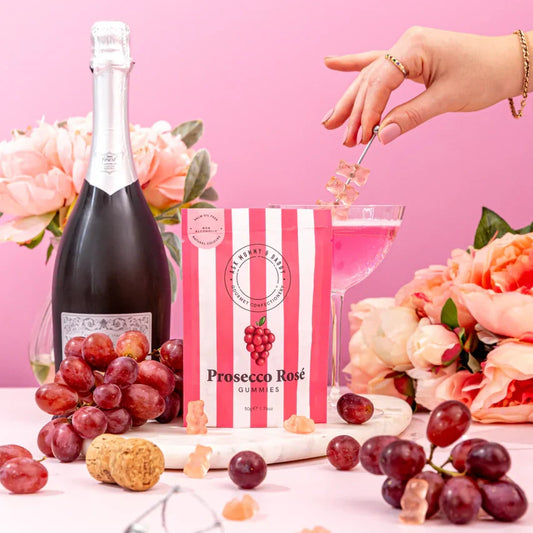 Prosecco Rose Gummies surrounded by grapes and a bottle of bubbly.