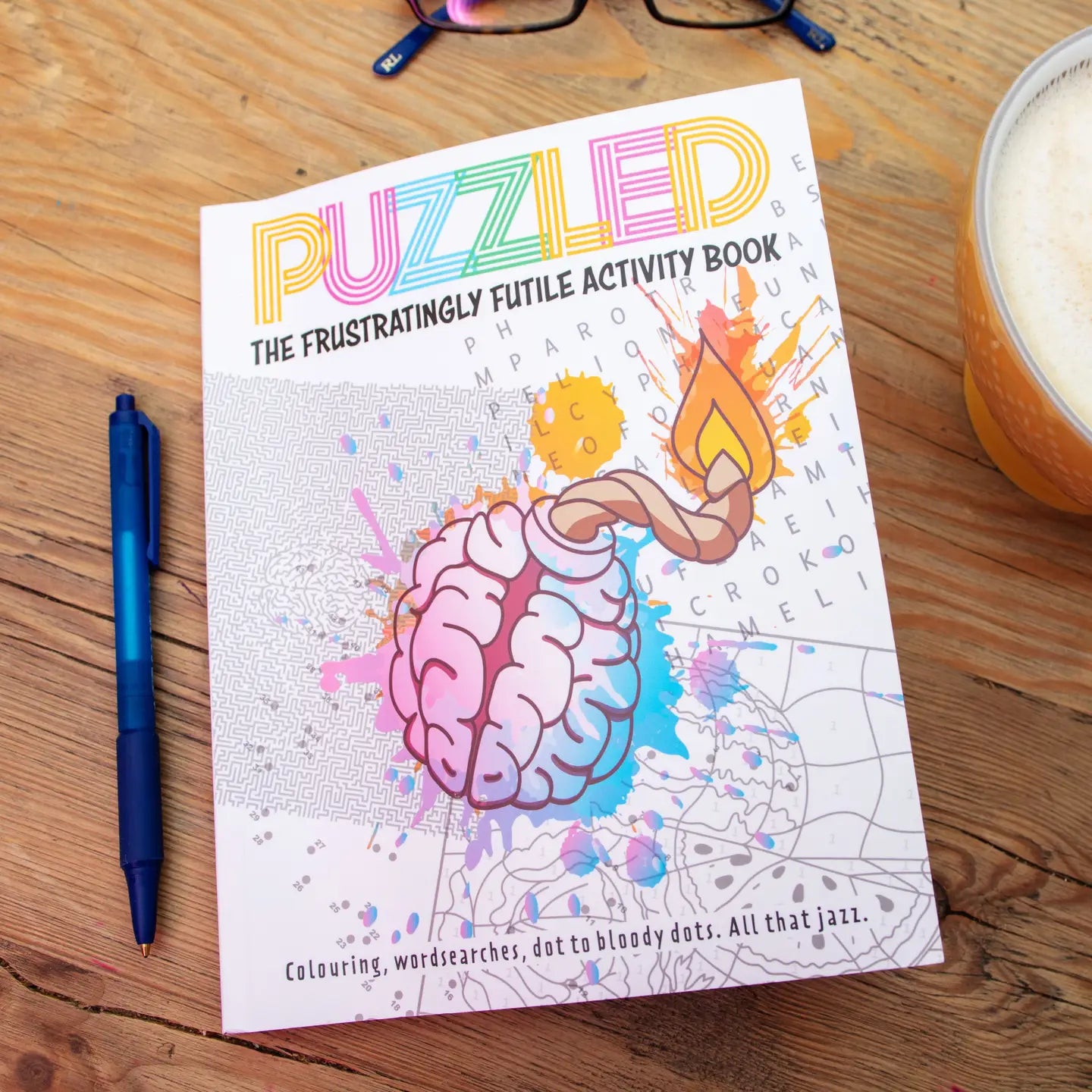Puzzled Book of Puzzling Puzzles with pen and glasses on wooden table.