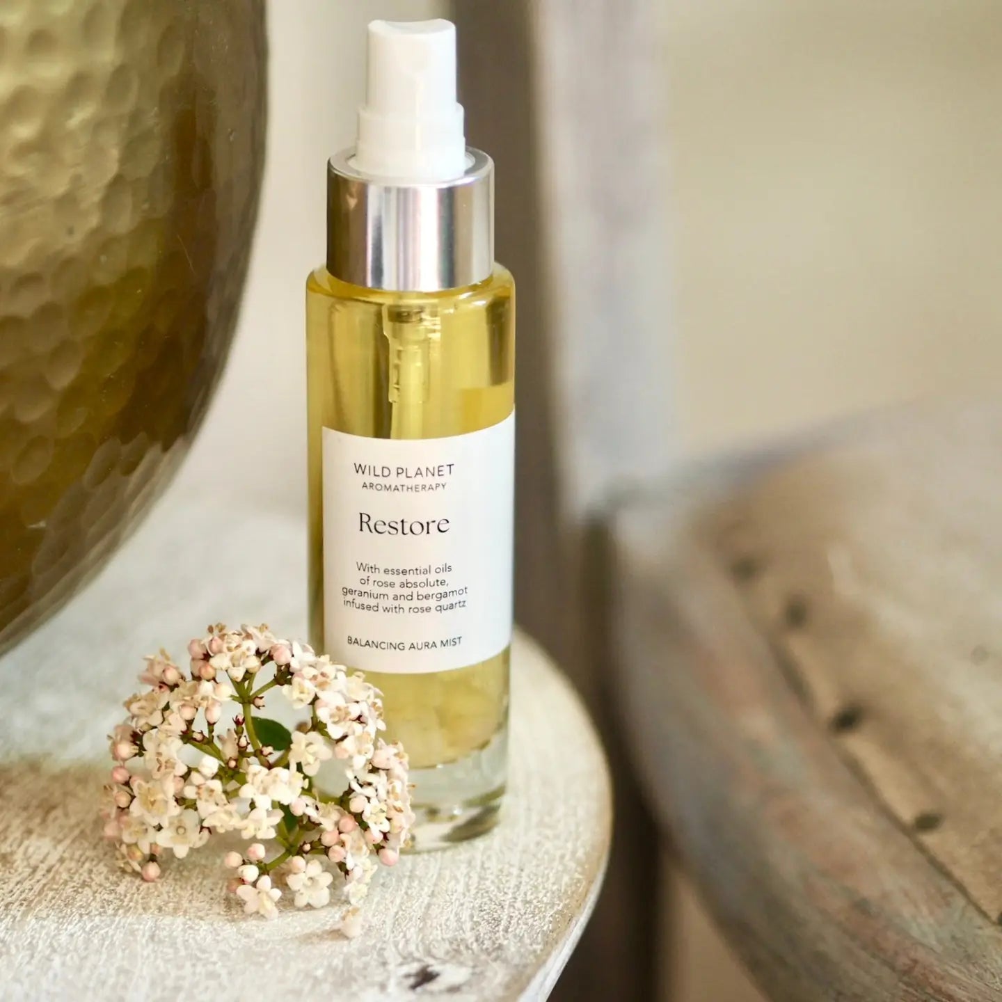 Restore Aura Mist Room Spray with rose quartz and essential oils on a table near flowers.