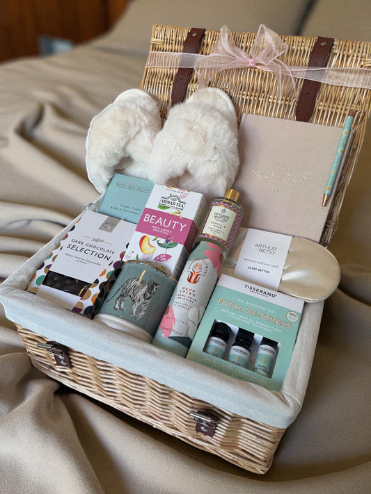 Self Care Luxe Hamper for Her including self care planner, sleep mask, Tisserand de-stress kit, bath oils, hand cream, tea, dark chocolate & fluffy slippers.