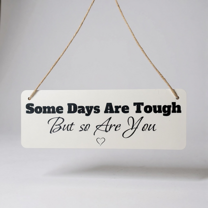 Motivational sign with text 'Some Days Are Tough But so Are You' on a plain background