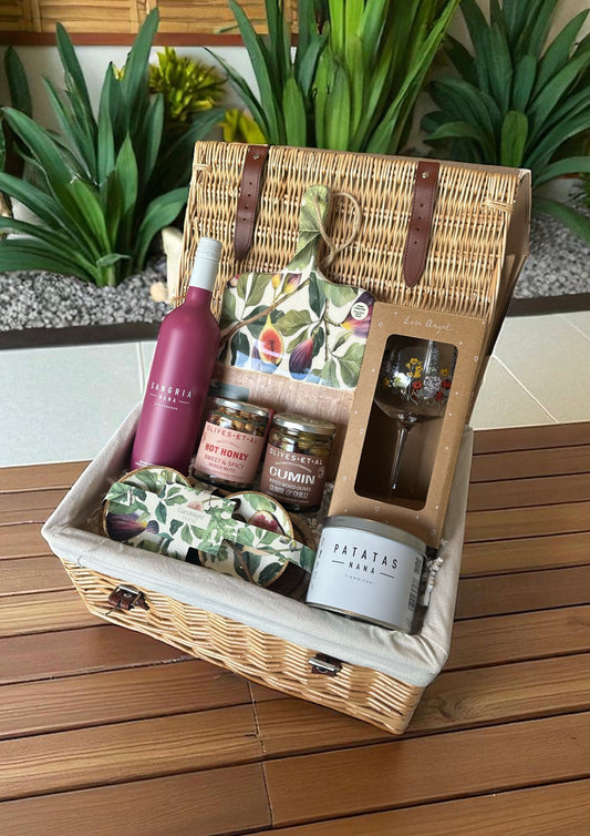 A sangria gift hamper featuring a bottle of sangria, a fig and olive wood serving board with dipping bowls, hot honey nuts, marinated olives, savoury crisp snacks, and a wildflower glass, arranged for gifting.