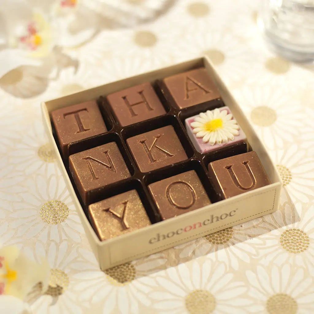 White Belgian chocolates spell “Thank You” with a mini daisy—sweet, simple, and thoughtful!