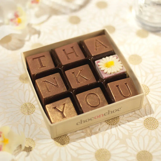White Belgian chocolates spell “Thank You” with a mini daisy—sweet, simple, and thoughtful!