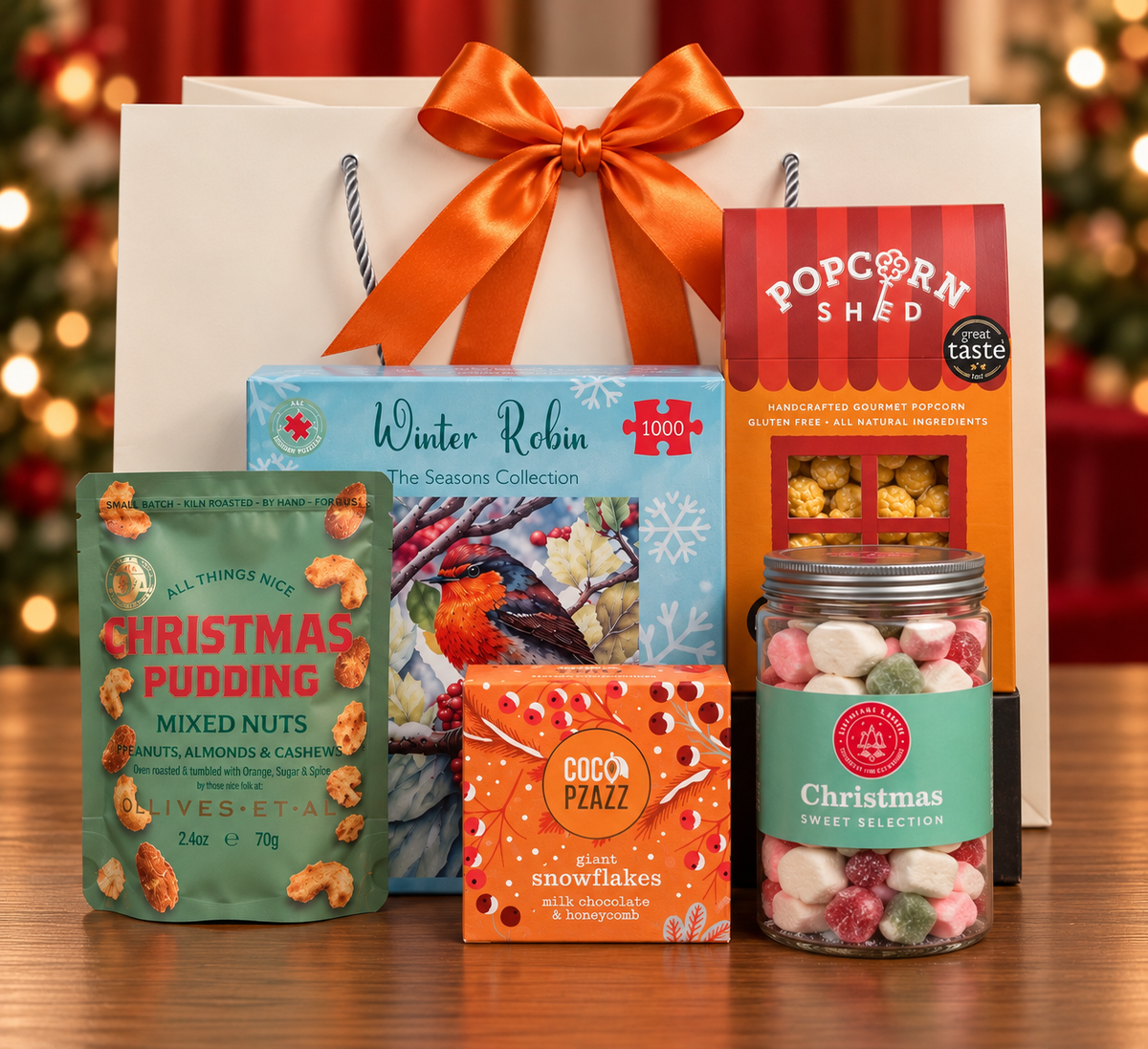 The Winter Robin Gift Bag on a wooden table, with a Winter Robin 1000 piece jigsaw puzzle, Popcorn Shed gourmet popcorn, Olives Et Al Christmas Pudding mixed nuts, Coco Pzazz milk chocolate and honeycomb snowflakes and a jar of Christmas sweets, in front of a white gift bag tied with a satin ribbon.