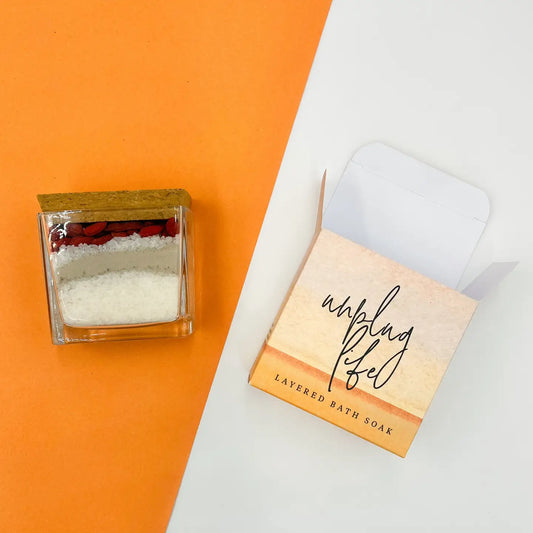Unplug Life layered bath soak with packaging on orange and white background.