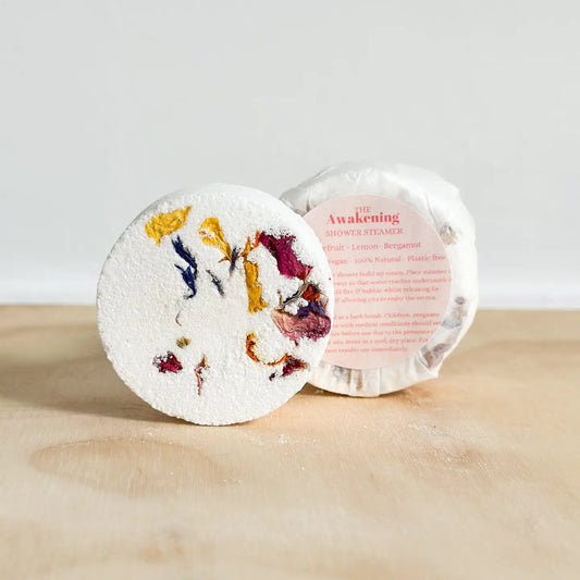 The Awakening Shower Steamer with dried flowers on top, displayed on a wooden surface.