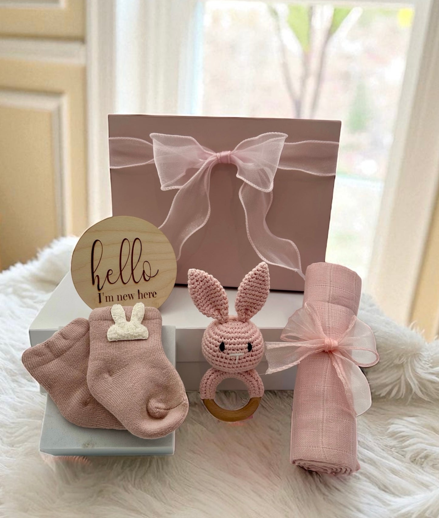 Baby Girl Gift Set featuring soft pink bunny socks, pink bunny rattle, gentle muslin cloth, and “Hello, I’m New Here” plaque for a newborn.